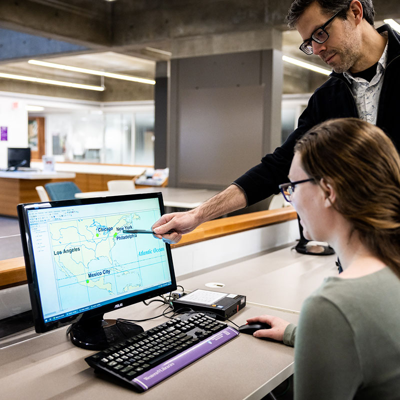 Staff member assisting a student on a library computer